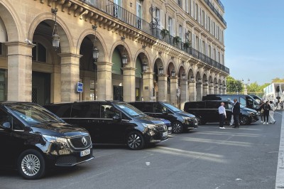 Miniature Regency Limo Coach #22 Alignement de véhicules noirs stationnés devant un bâtiment en pierre avec arcades, sous un ciel dégagé.