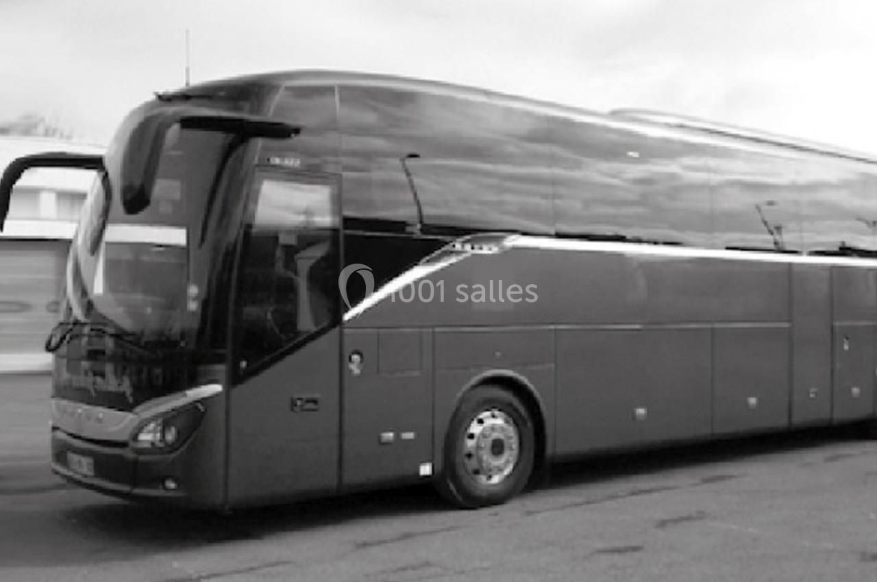 Autocar stationné sur une aire, vu de profil, avec un ciel nuageux en arrière-plan.