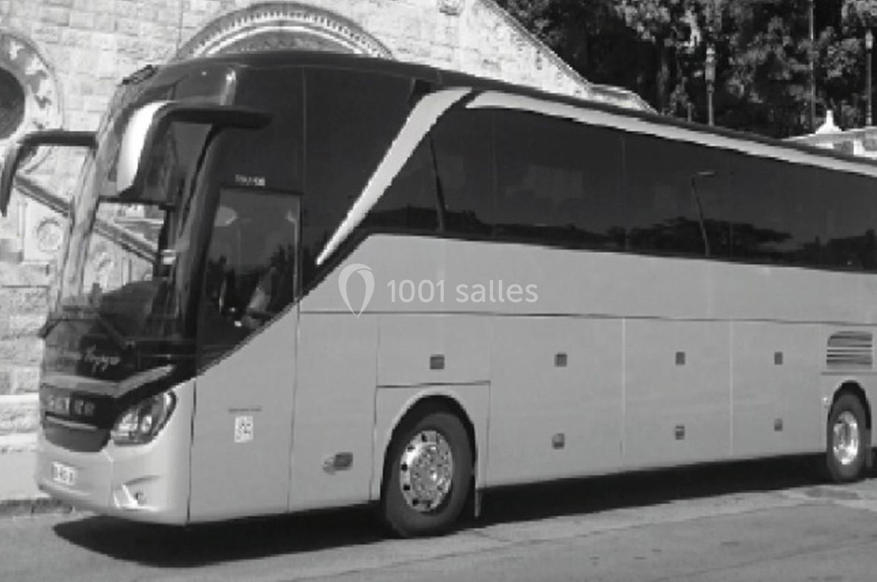 Autocar stationné devant un bâtiment en pierre avec des arches et des arbres en arrière-plan.