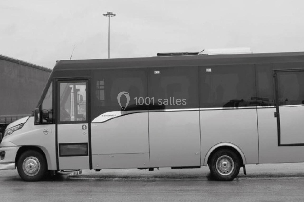 Minibus stationné sur une surface pavée, vu de profil, avec un bâtiment industriel en arrière-plan.