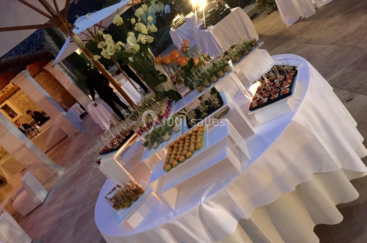 Buffet élégant en extérieur avec tables rondes garnies de verrines, fleurs et amuse-bouches sous des parasols.