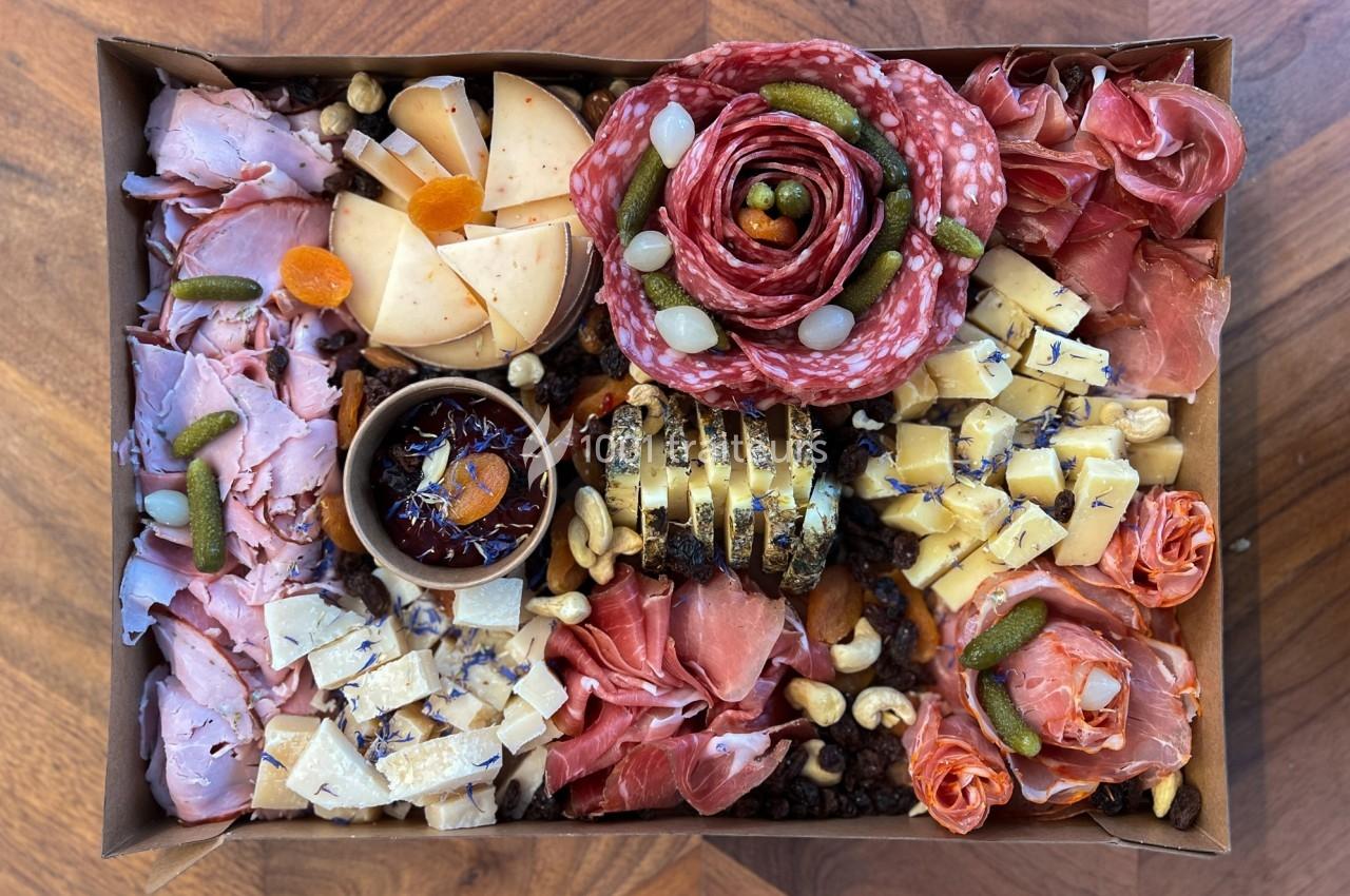 Plateau garni de charcuteries, fromages variés, fruits secs, cornichons et confiture, présenté sur une table en bois.