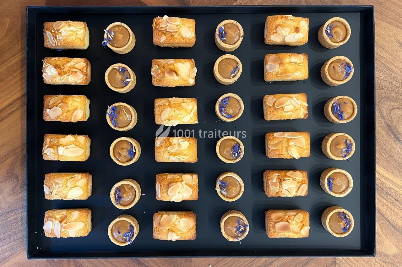 Plateau de mignardises composé de financiers aux amandes et de tartelettes au caramel décorées de fleurs bleues.