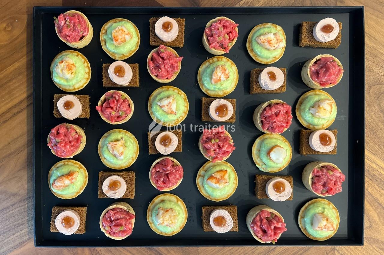 Plateau de canapés variés comprenant des bouchées au tartare, au fromage et aux crevettes, disposées en rangées.