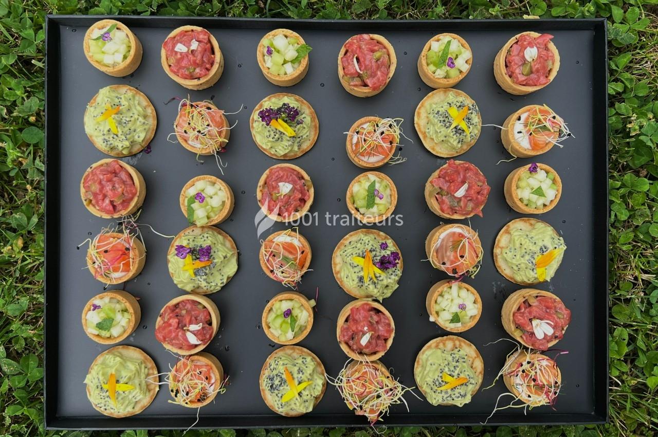 Plateau de bouchées apéritives variées disposées sur un fond noir, posé sur de l'herbe verte.