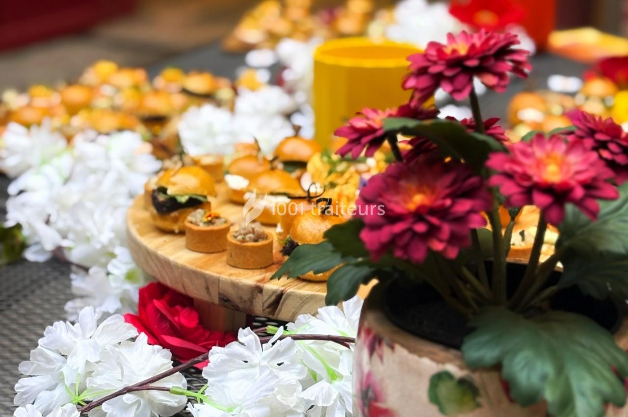 Plateau de bouchées apéritives sur une table décorée de fleurs blanches et rouges, avec un pot de fleurs au premier plan.