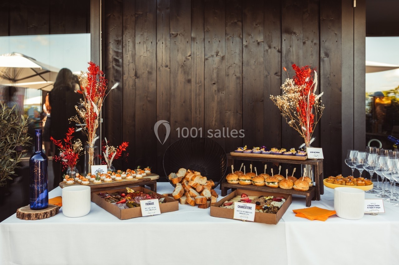 Buffet avec plateaux de bouchées variées, pains, verrines et décorations florales sur une table blanche.