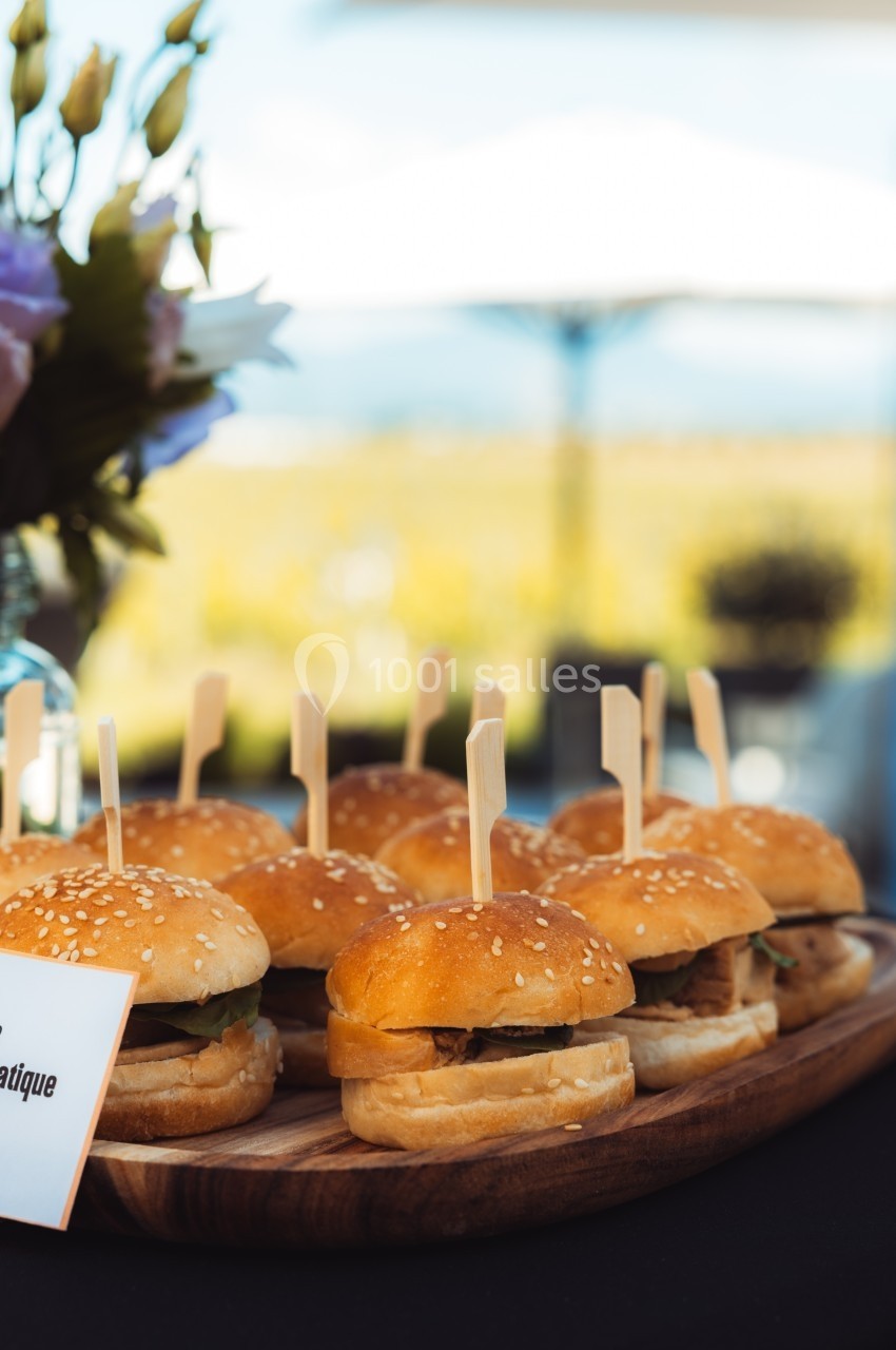 Plateau de mini-burgers garnis, présentés sur une table en extérieur avec un décor flou en arrière-plan.