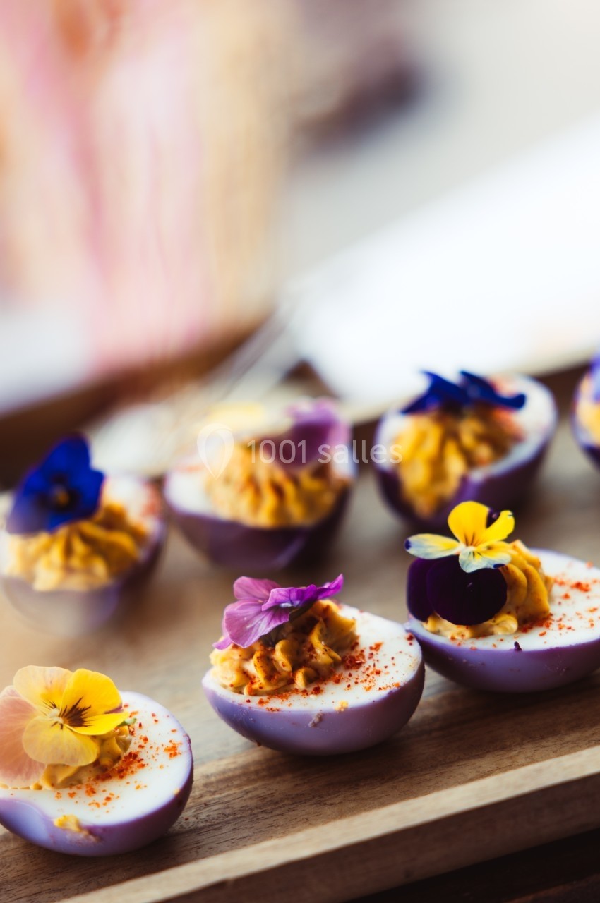 Œufs farcis violets garnis de fleurs comestibles colorées, présentés sur un plateau en bois.