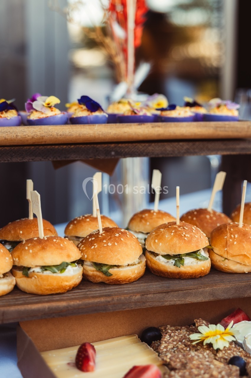 Plateau de mini-burgers garnis de légumes frais, accompagné de desserts et d'amuse-bouches sur une table de buffet.