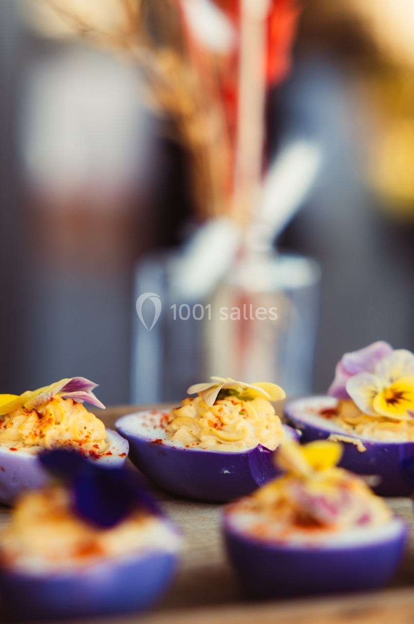 Œufs farcis présentés dans des coquilles violettes, décorés de fleurs comestibles et d'épices.