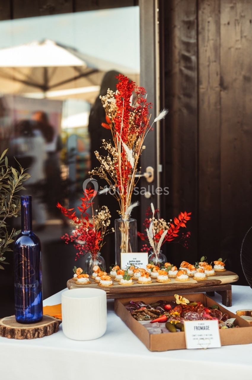 Table décorée avec des fleurs séchées, des amuse-bouches, une bouteille bleue et un plateau de fromages et fruits.