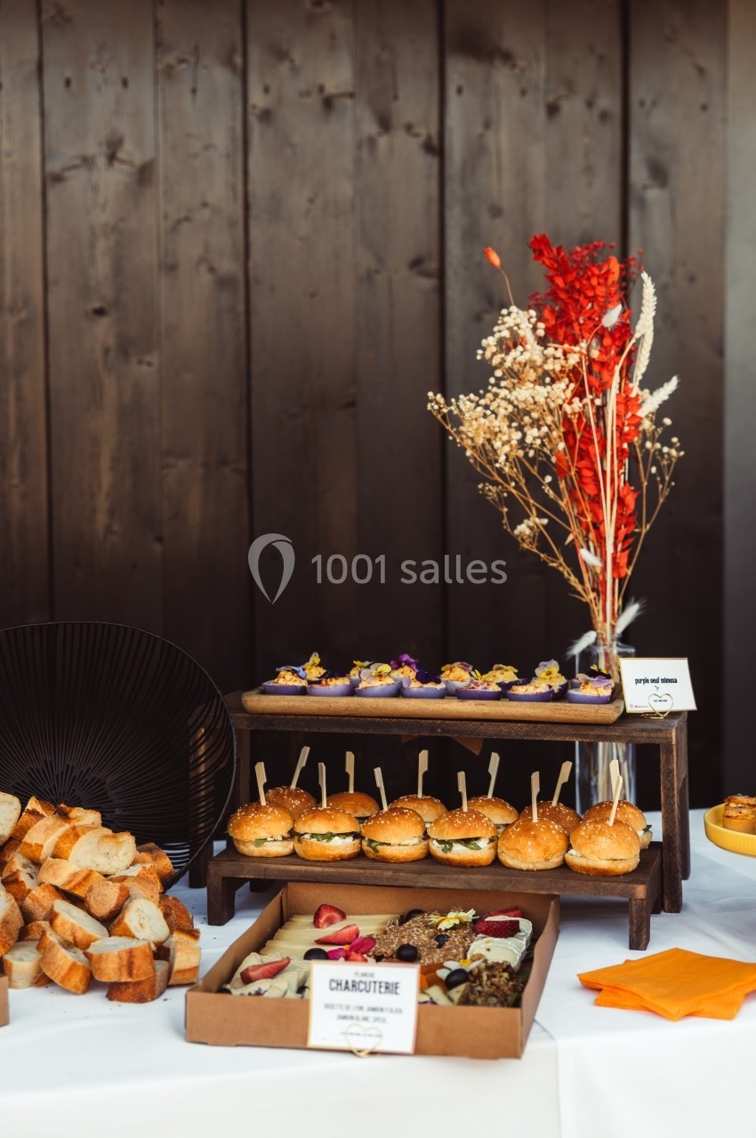 Buffet avec pains, mini-burgers, charcuterie et fleurs séchées en décoration sur une table blanche.