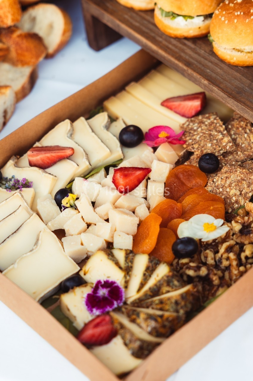 Plateau de fromages variés avec fruits secs, noix, tranches de pain et décorations florales comestibles.