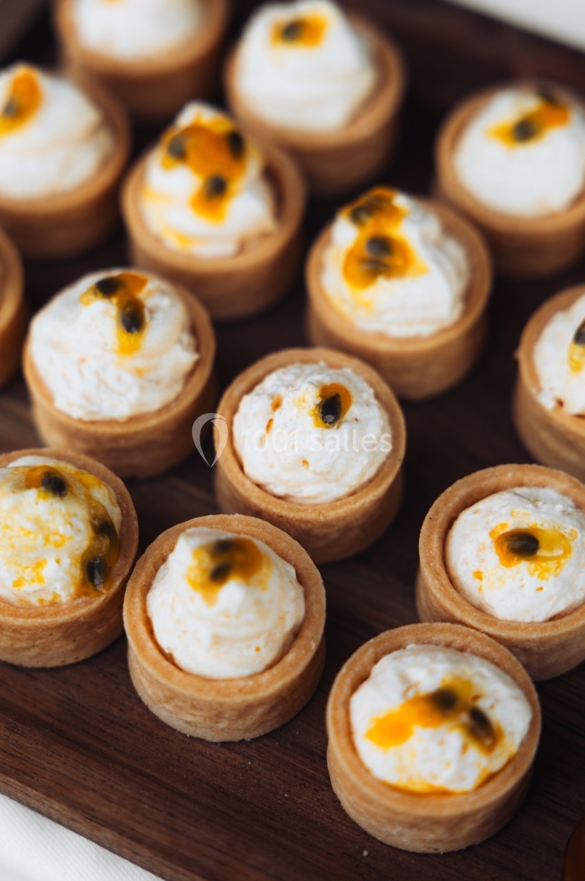 Tartelettes garnies de crème blanche et décorées de morceaux de fruit de la passion, présentées sur un plateau en bois.