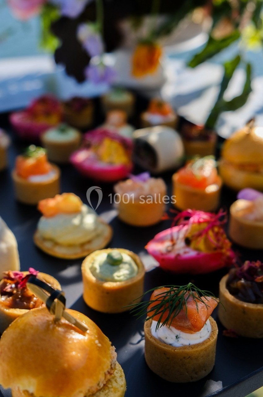 Plateau de bouchées apéritives variées, comprenant des tartes salées et des garnitures colorées, disposé sur une table.