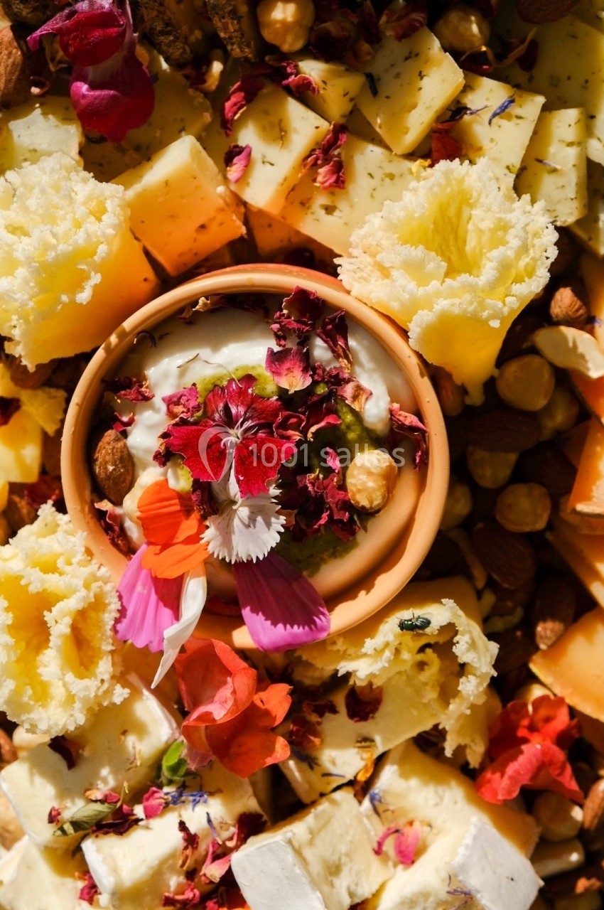 Plateau de fromages variés décoré de fleurs comestibles, fruits secs et herbes, présenté en gros plan.