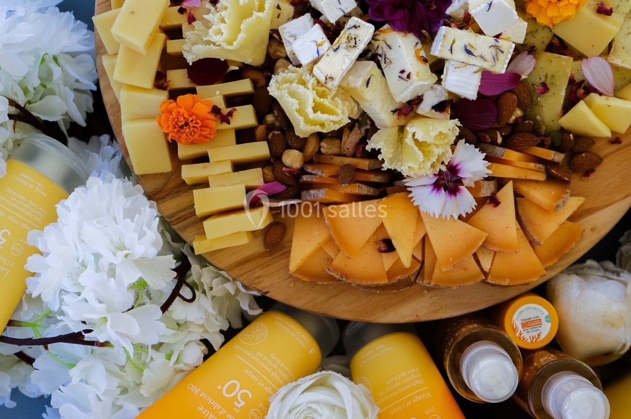 Plateau de fromages variés avec fleurs comestibles, accompagné de bouteilles de crème solaire et décoré de fleurs blanches.
