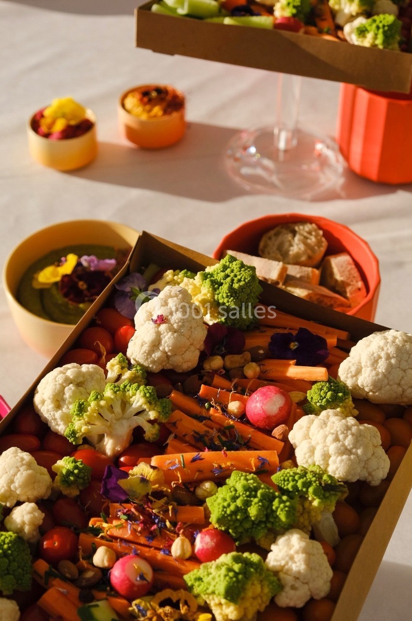 Plateaux de légumes frais colorés avec choux-fleurs, carottes, radis et garnitures florales sur une table lumineuse.