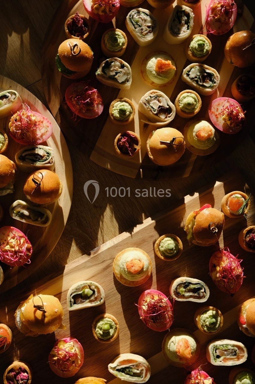 Plateaux de bouchées variées comprenant mini-burgers, roulés, et amuse-bouches colorés sur une table en bois.
