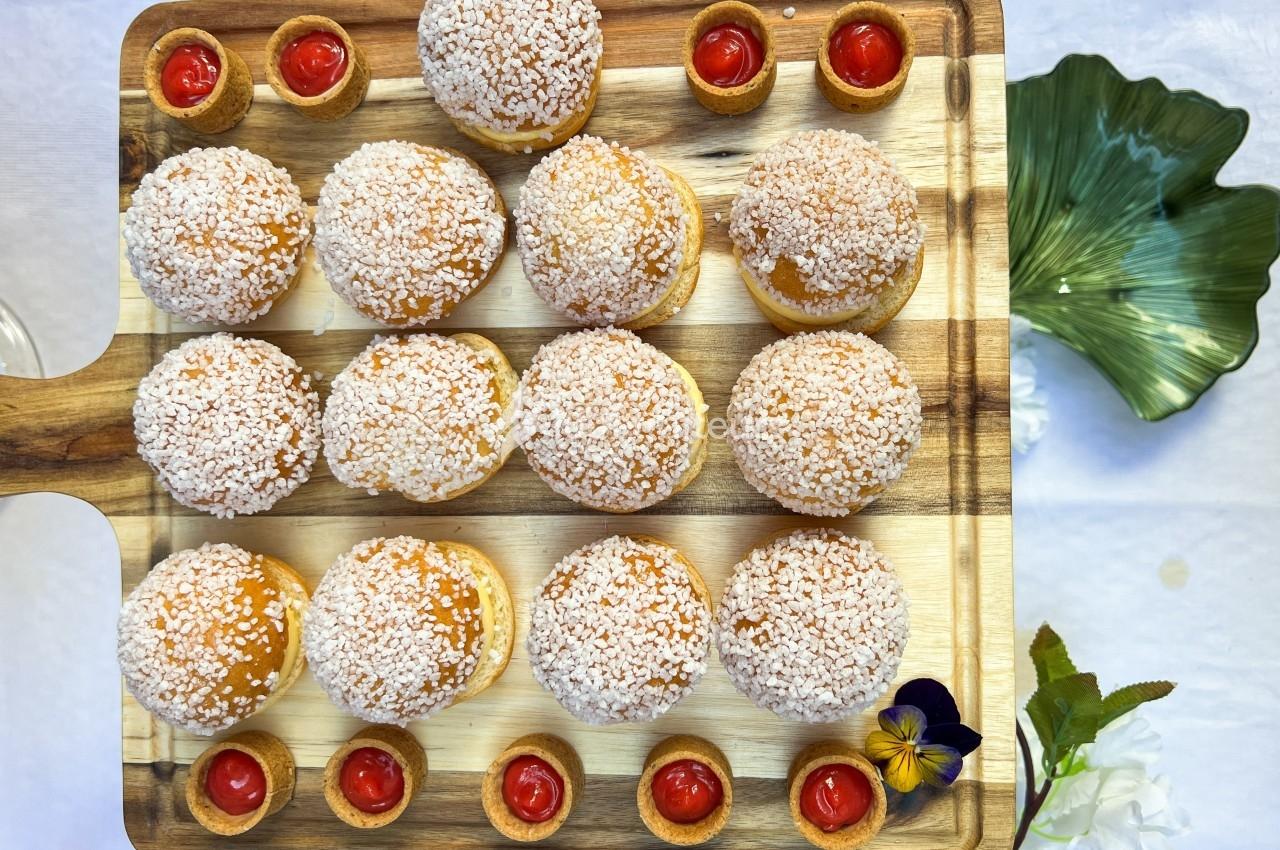 Plateau en bois avec des chouquettes saupoudrées de sucre et des petites coupelles de sauce rouge, décoré de fleurs.