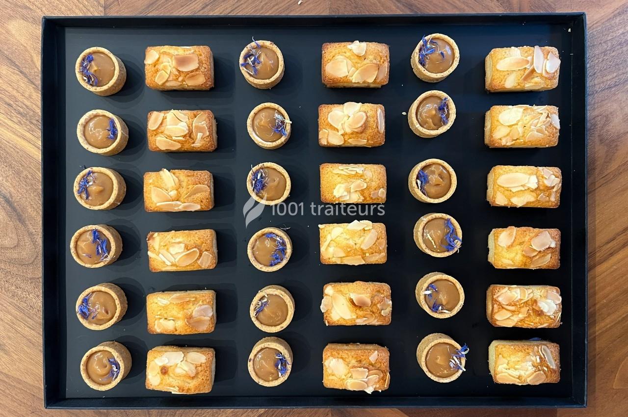 Plateau de mignardises comprenant des tartelettes au caramel et des financiers aux amandes, disposés en rangées.