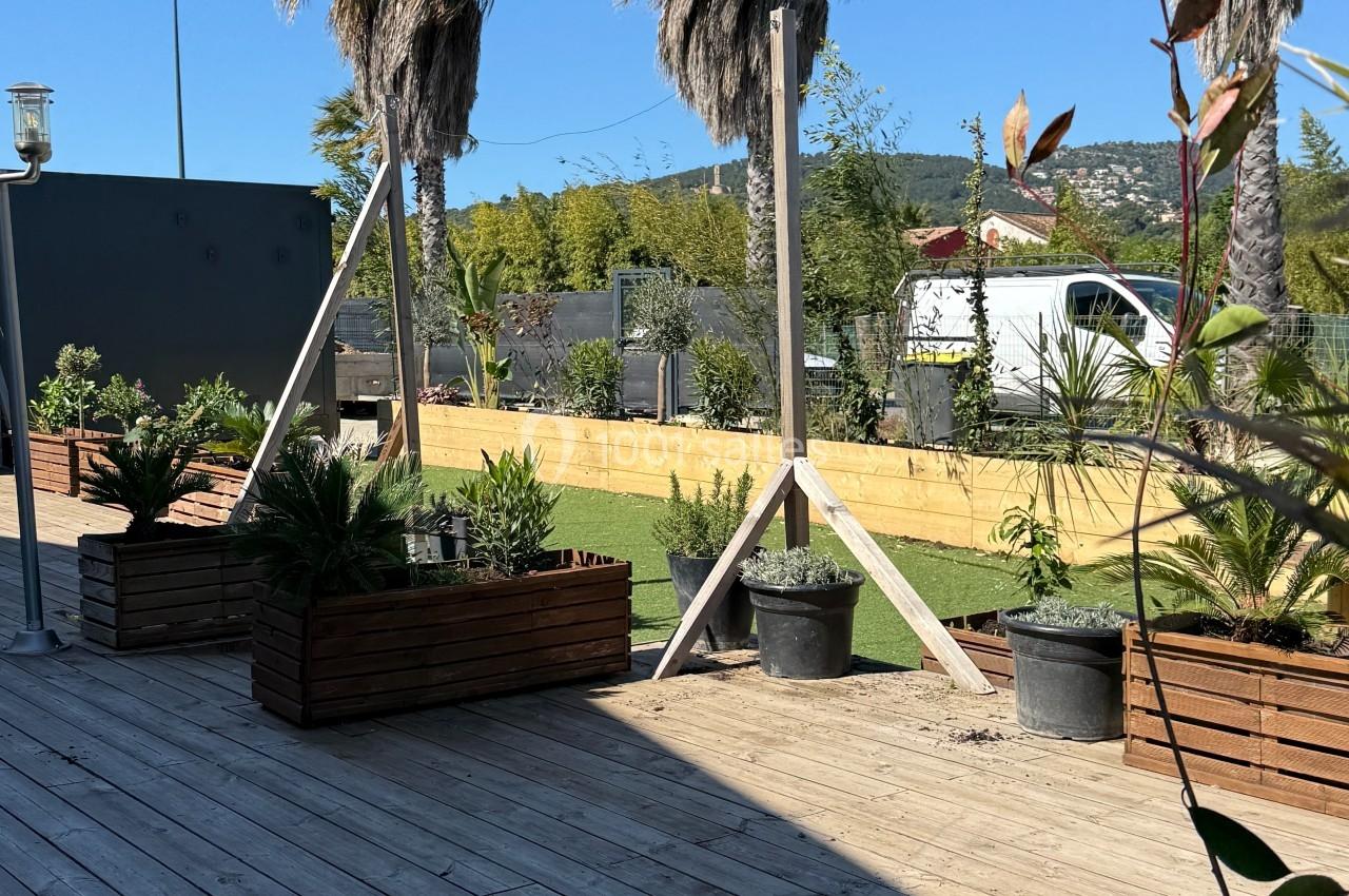 Terrasse en bois avec des jardinières, des palmiers et une vue dégagée sur un espace extérieur ensoleillé.
