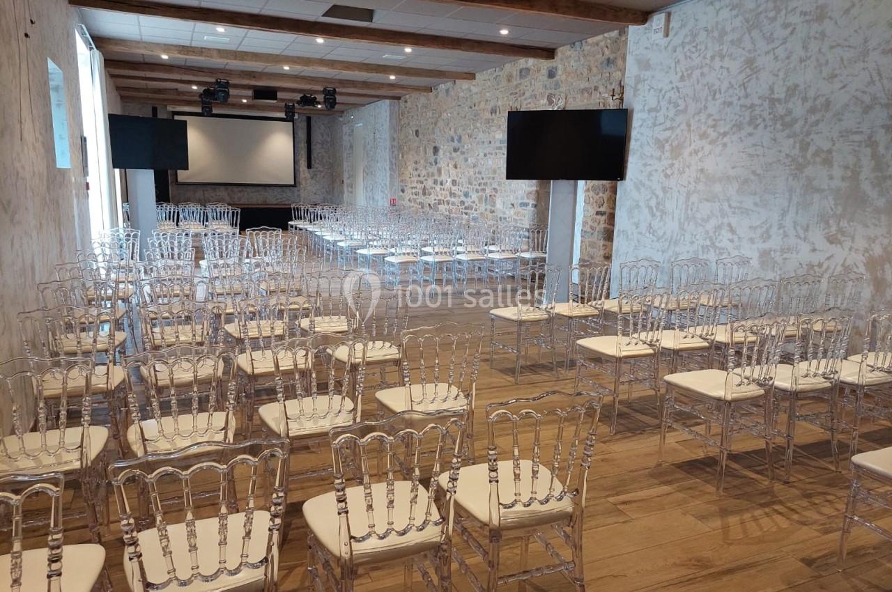Salle de conférence avec des chaises transparentes alignées, écran de projection et murs en pierre apparente.