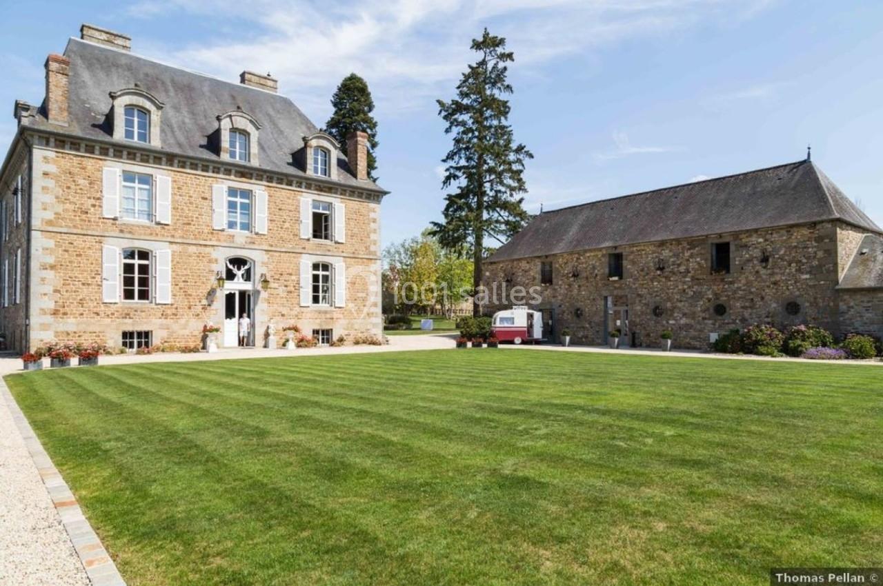 Manoir en pierre avec pelouse bien entretenue, accompagné d'une grange et d'une caravane rouge sous un ciel dégagé.