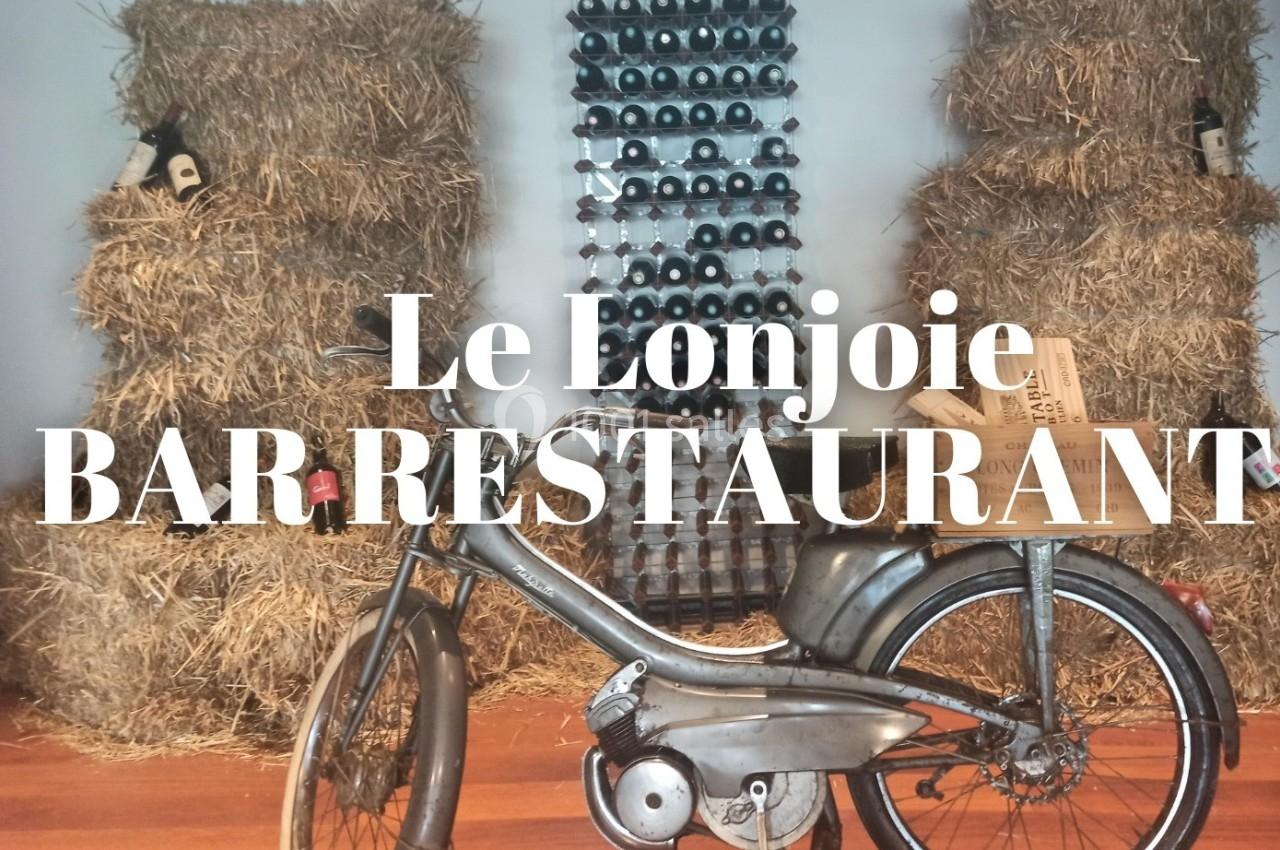 Une vieille mobylette devant des bottes de paille et un présentoir de bouteilles de vin dans un décor rustique.
