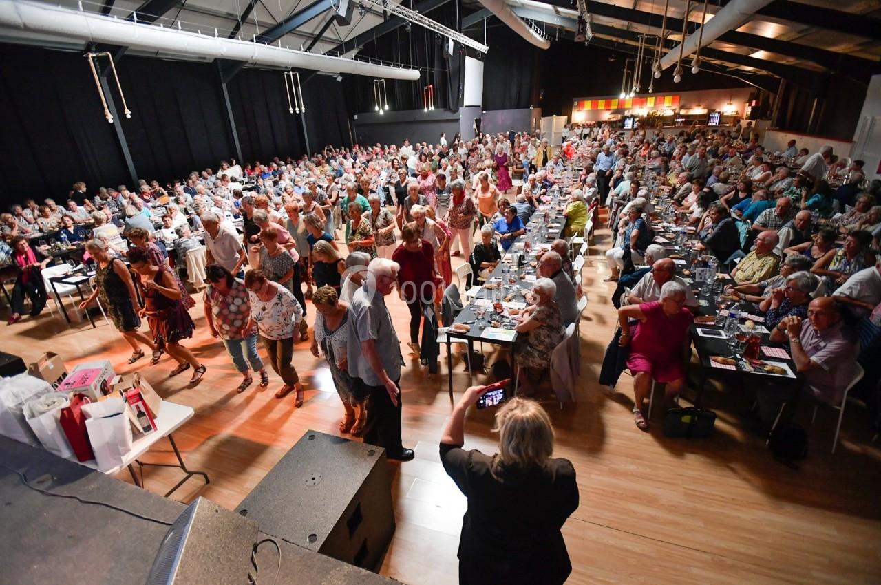Salle comble avec des personnes debout et assises participant à un événement festif dans un espace intérieur lumineux.