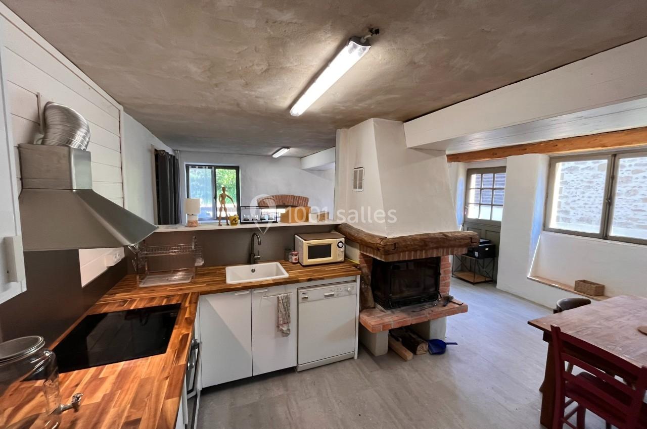 Cuisine lumineuse avec plan de travail en bois, évier blanc, cheminée en pierre et table à manger en arrière-plan.