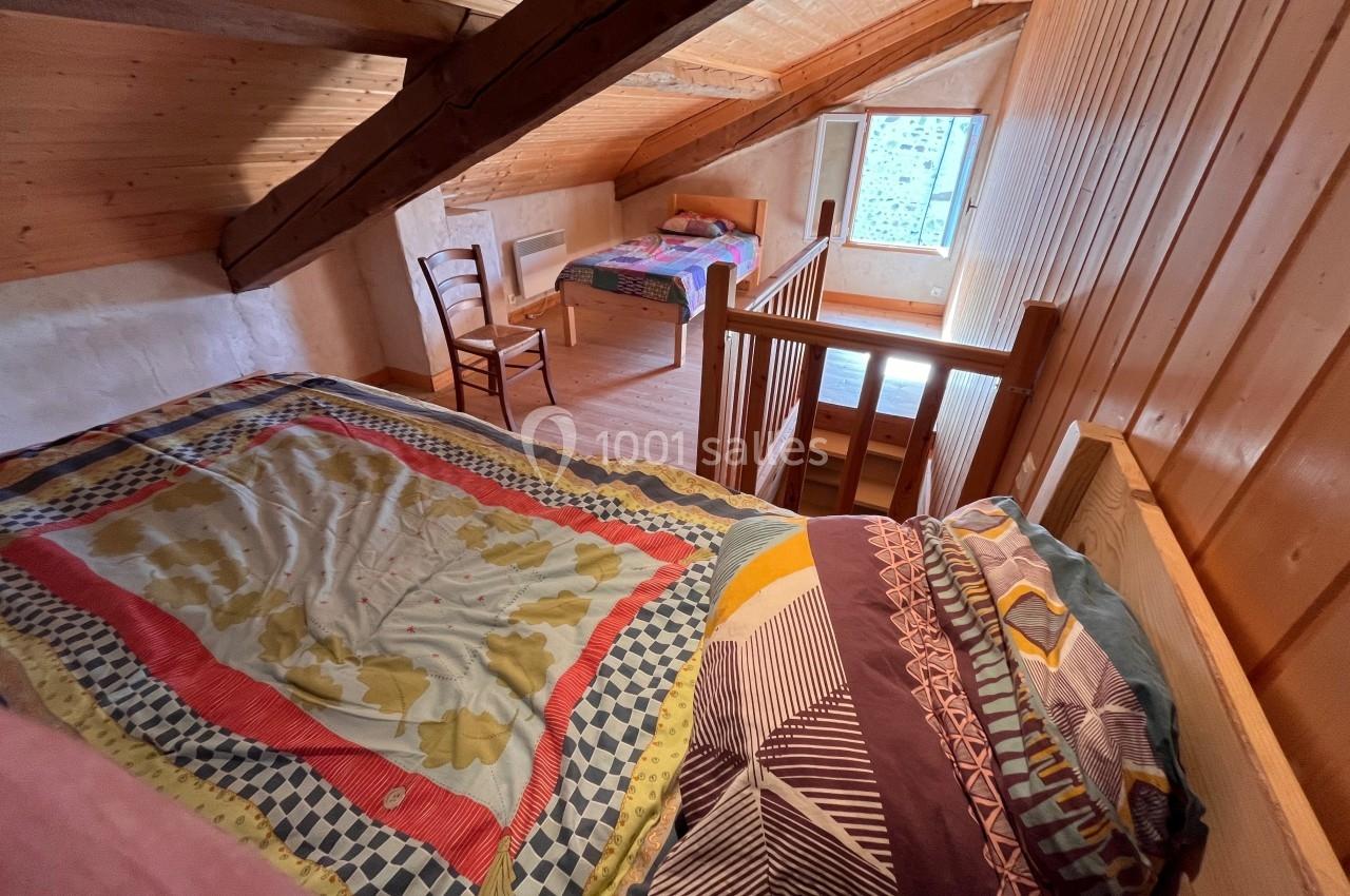 Chambre mansardée en bois avec deux lits, une chaise et une fenêtre laissant entrer la lumière naturelle.