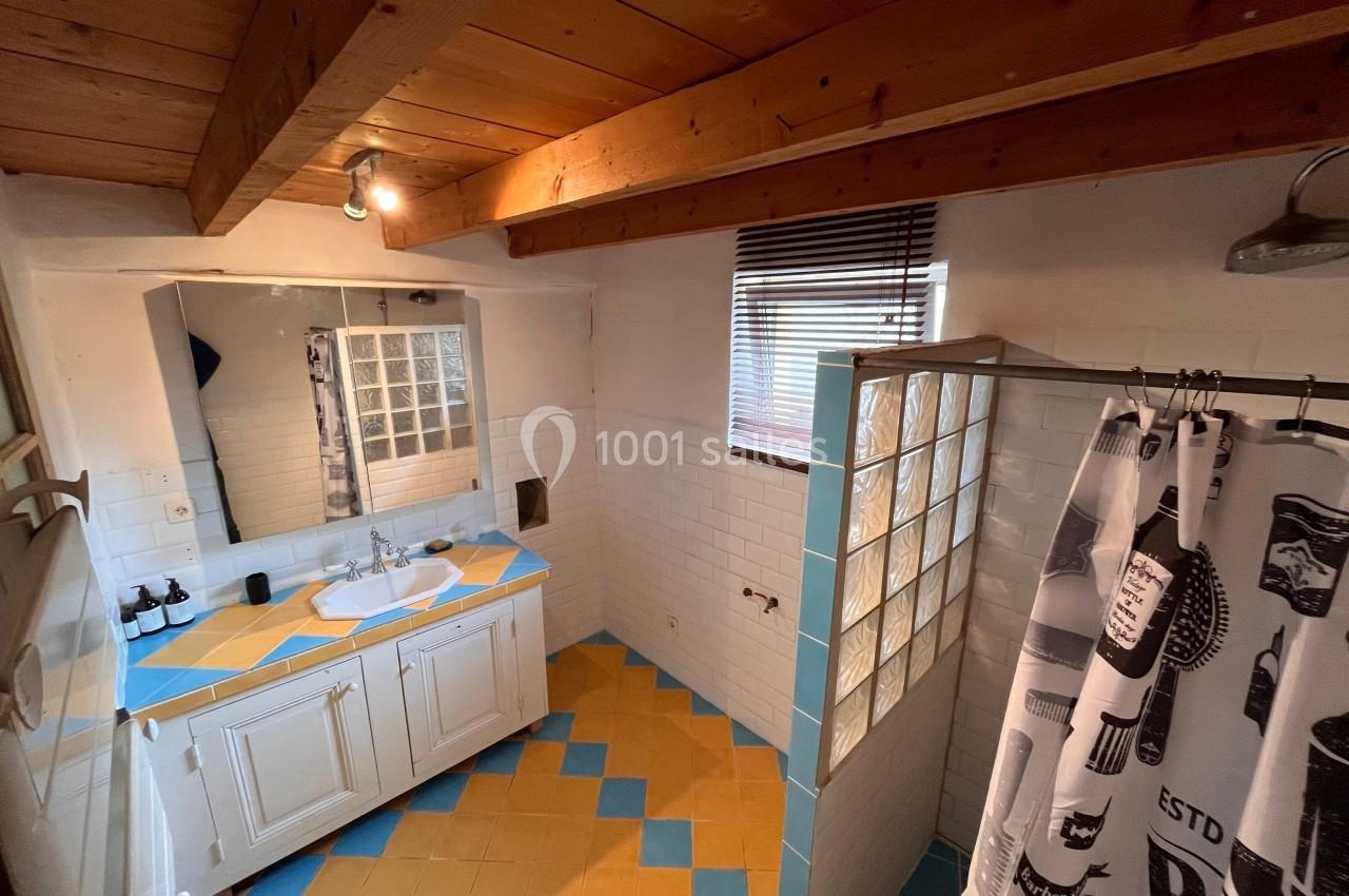 Salle de bain avec plafond en bois, carrelage coloré, douche avec rideau et lavabo sur meuble blanc.