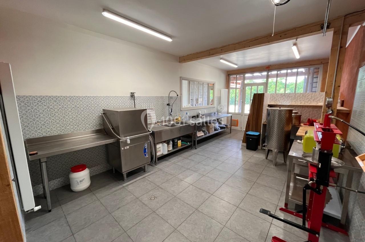 Cuisine professionnelle avec plan de travail en inox, évier, carrelage mural et équipements divers, éclairée par des néons.