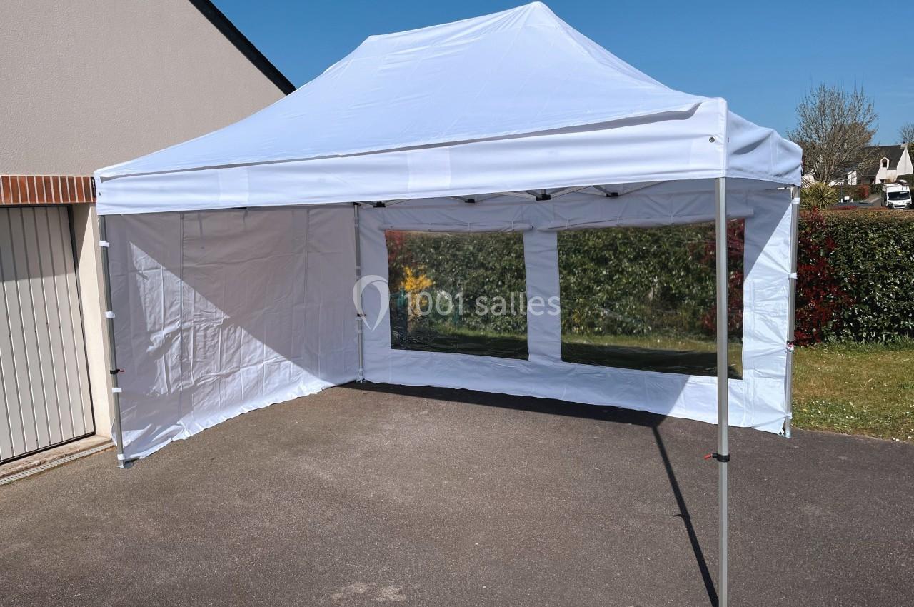 Tente blanche montée dans une cour, avec parois latérales et fenêtres transparentes donnant sur un jardin.