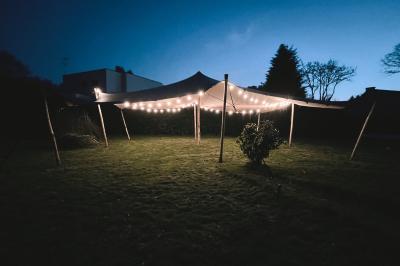 Tente beige éclairée par des guirlandes lumineuses, installée dans un jardin au coucher du soleil.