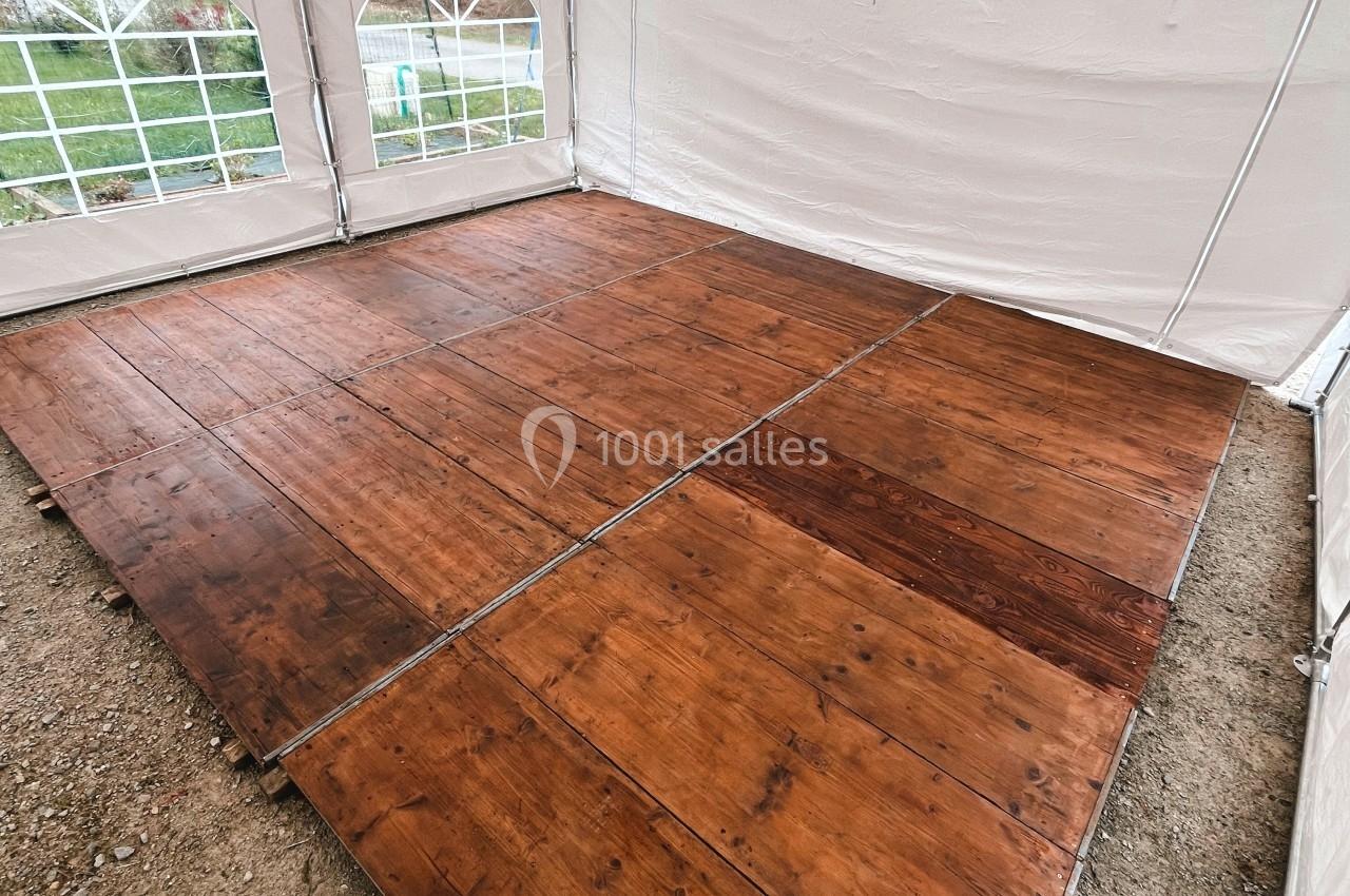 Plancher en bois installé sous une tente blanche avec des fenêtres arrondies, posé sur un sol en gravier.