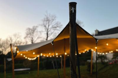 Tente beige éclairée par des guirlandes lumineuses, installée dans un jardin au coucher du soleil.