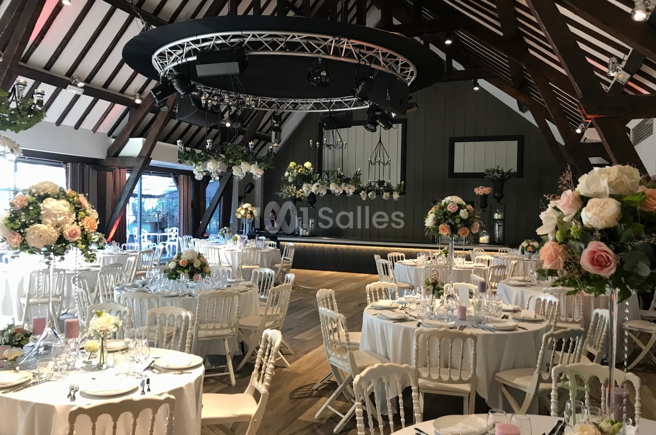 Salle de réception décorée avec des tables rondes, des chaises blanches et des compositions florales élégantes.