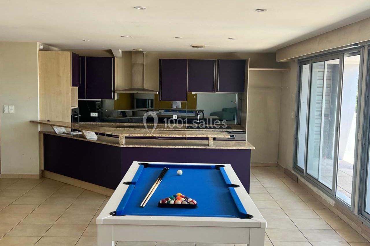 Cuisine ouverte moderne avec comptoir en marbre, meubles violets et table de billard blanche au premier plan.