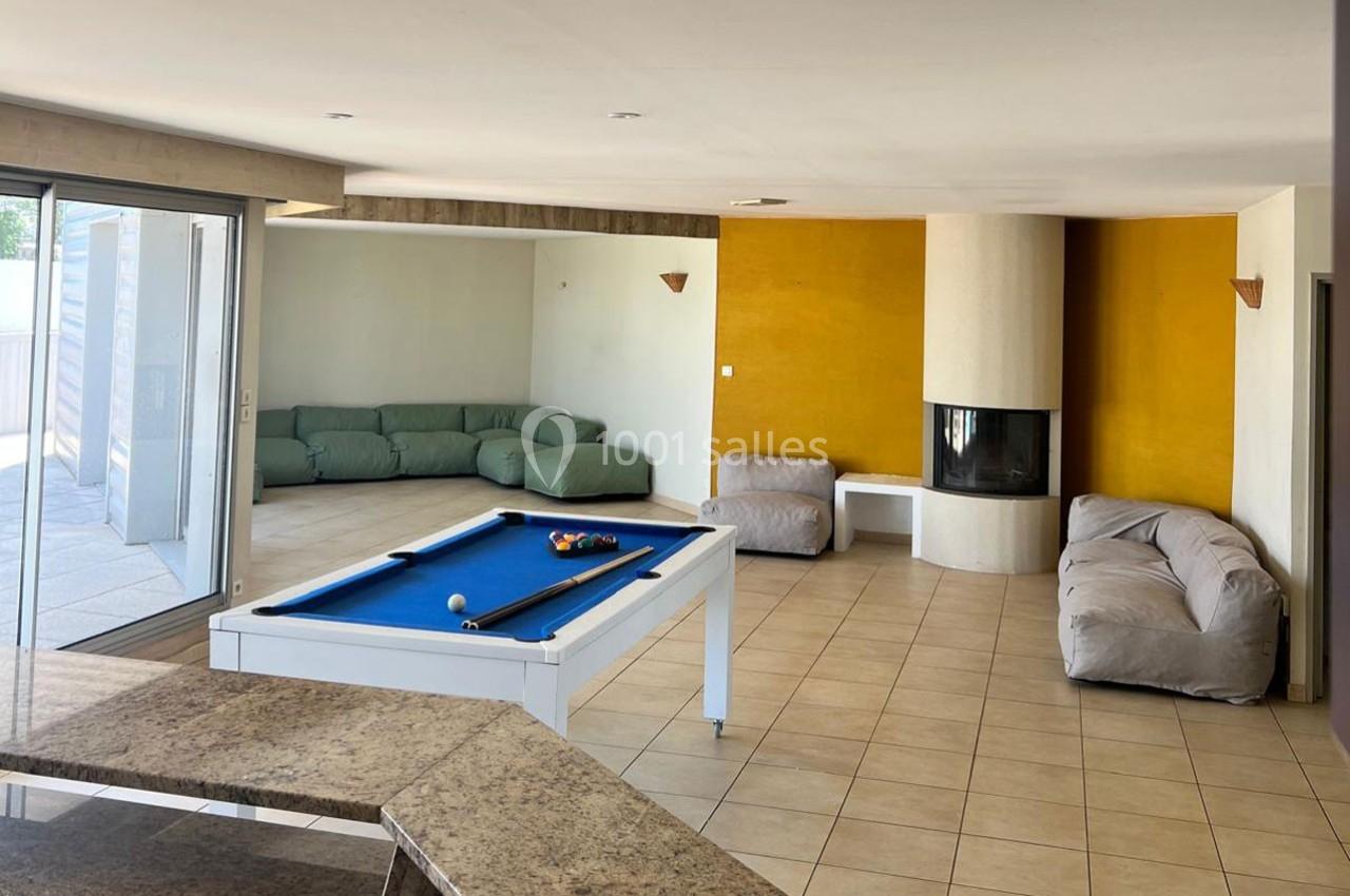 Salle de séjour lumineuse avec table de billard, canapés, cheminée moderne et accès à une terrasse extérieure.