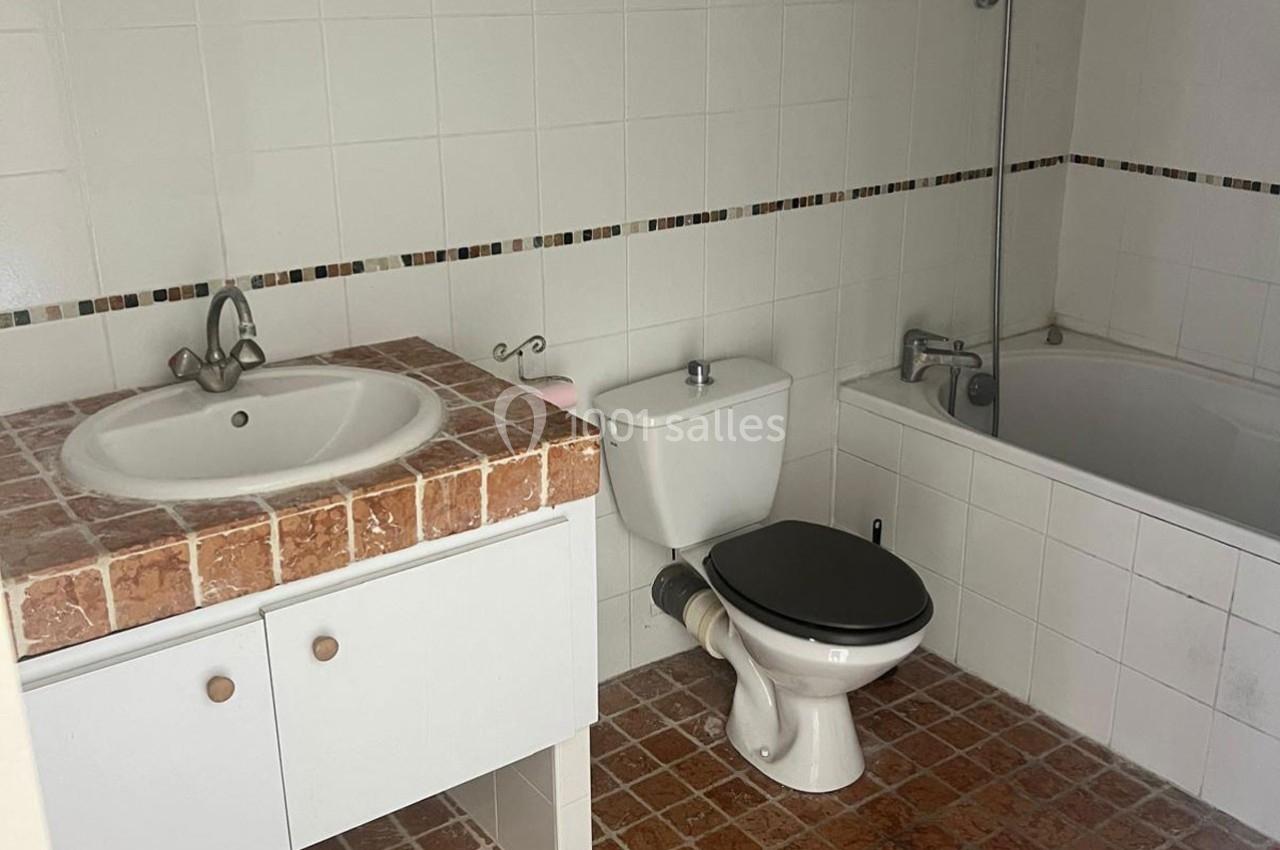 Salle de bain avec lavabo sur plan en marbre, toilettes blanches et baignoire équipée d'une douche.