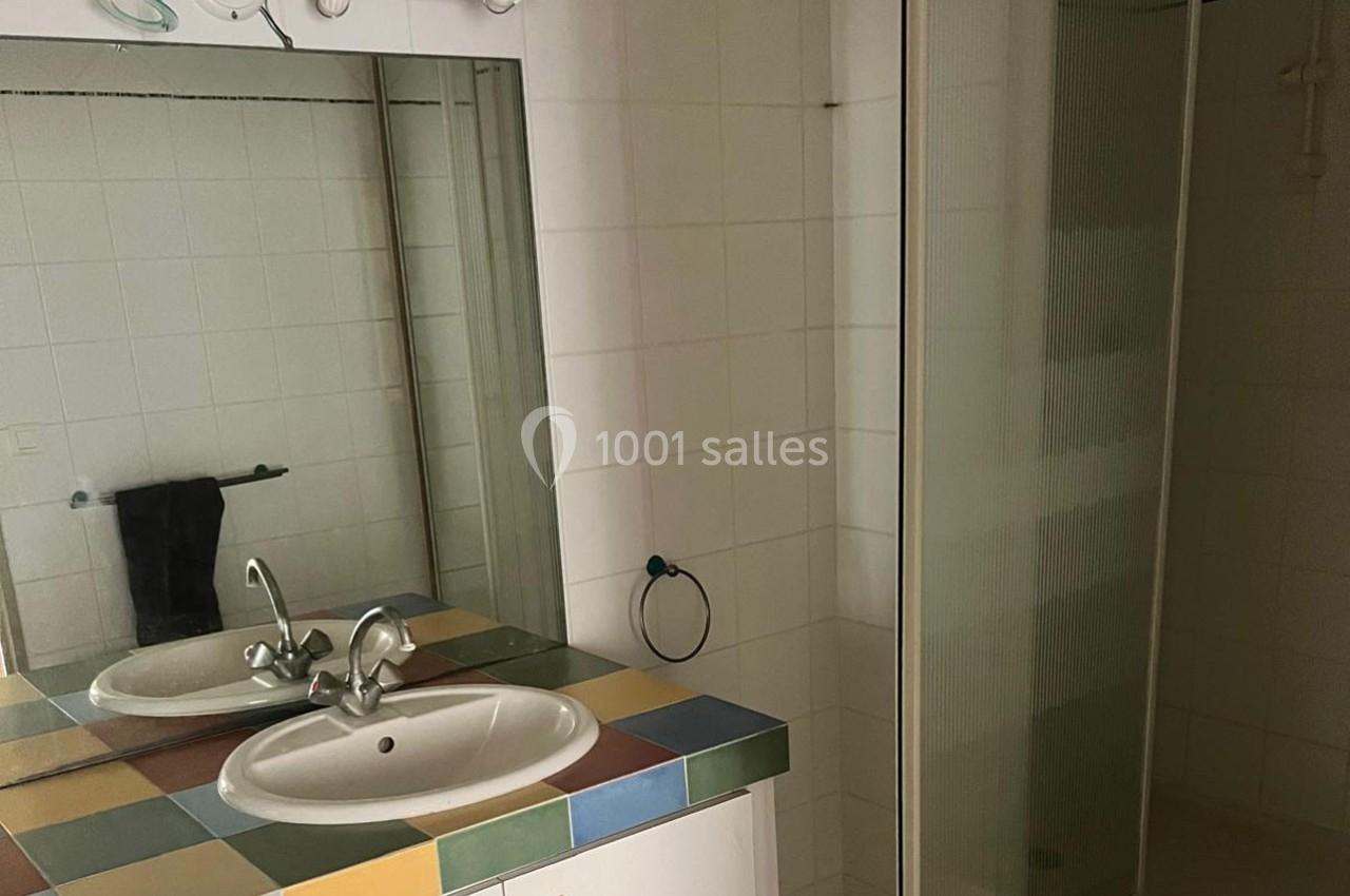 Salle de bain avec lavabo sur meuble coloré, miroir, serviette suspendue et cabine de douche vitrée.