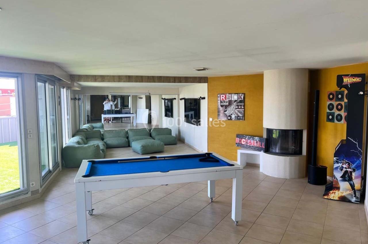 Salle lumineuse avec billard blanc, poufs verts, cheminée moderne et décorations murales colorées.