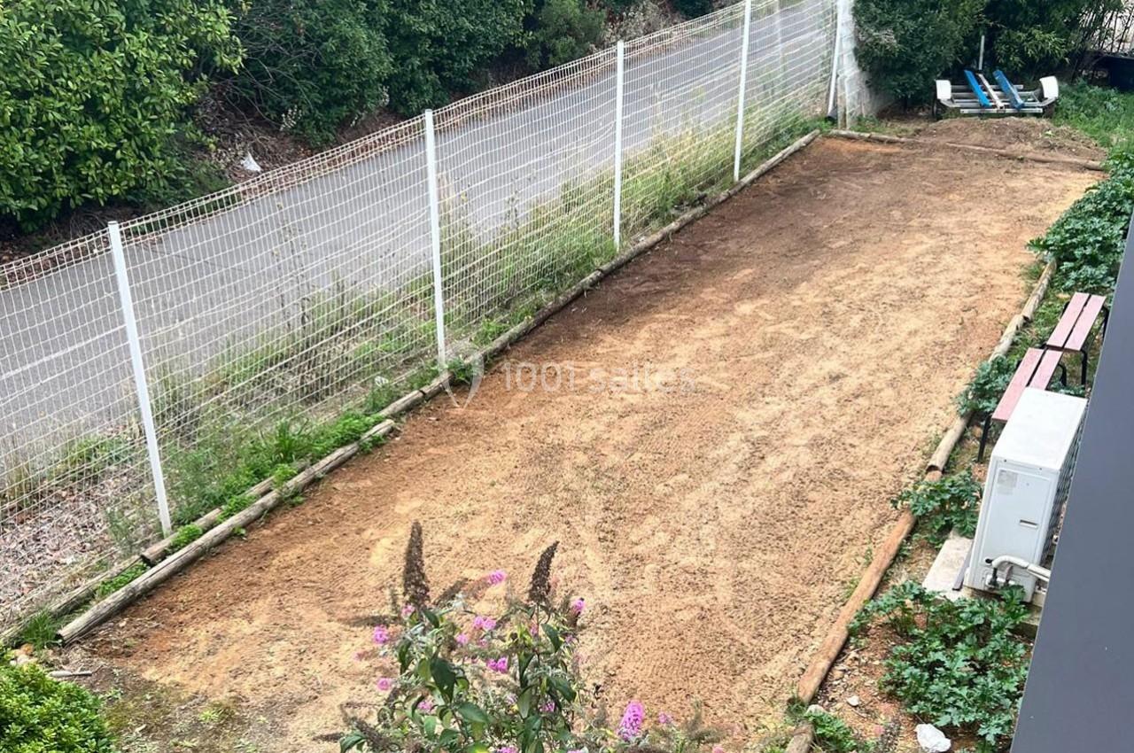 Terrain de jardin rectangulaire fraîchement préparé, entouré de végétation, d'une clôture et d'un banc en bois.