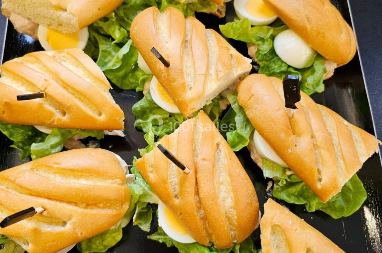 Plateau de mini-sandwichs garnis de salade, œufs durs et sauce, présentés sur un fond noir.