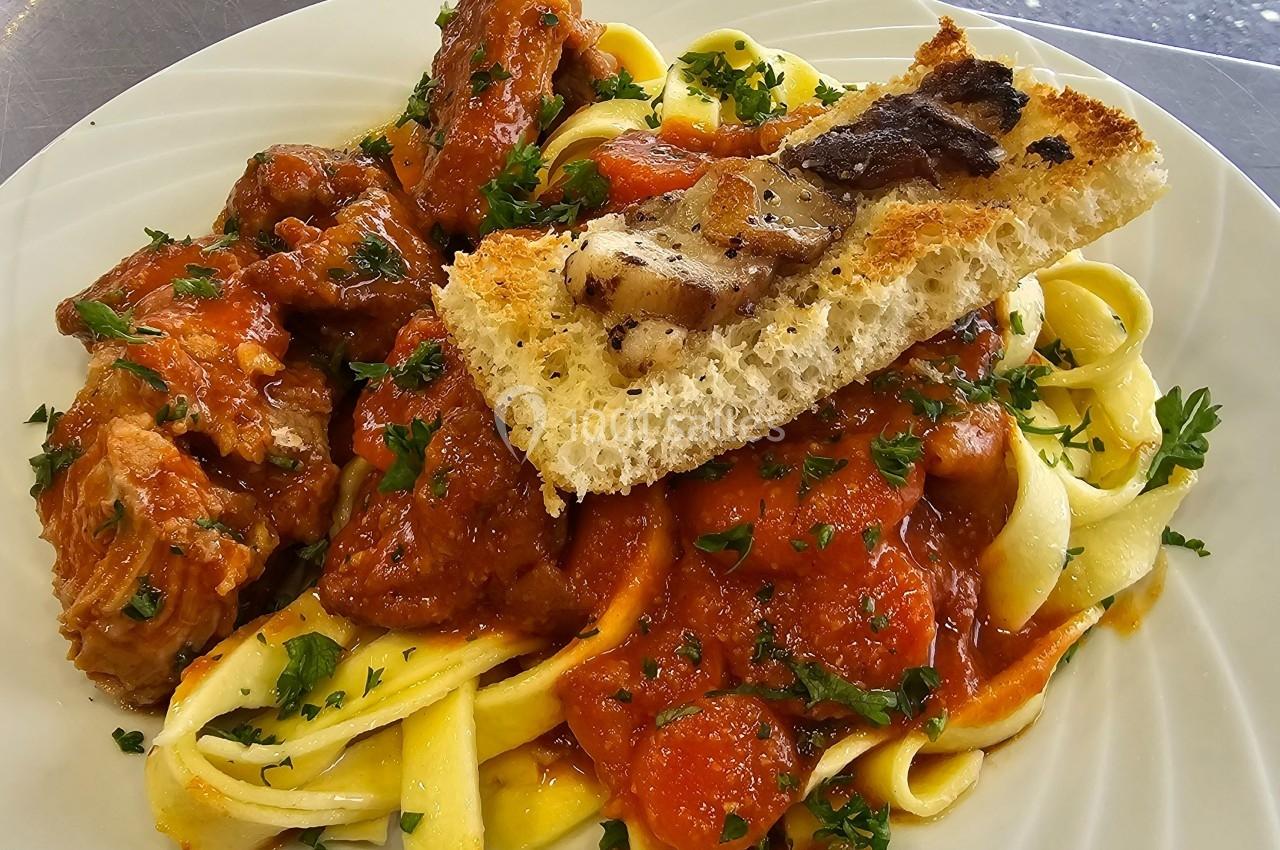 Assiette de tagliatelles fraîches avec sauce tomate, morceaux de viande, persil frais et croûton garni de lard grillé.