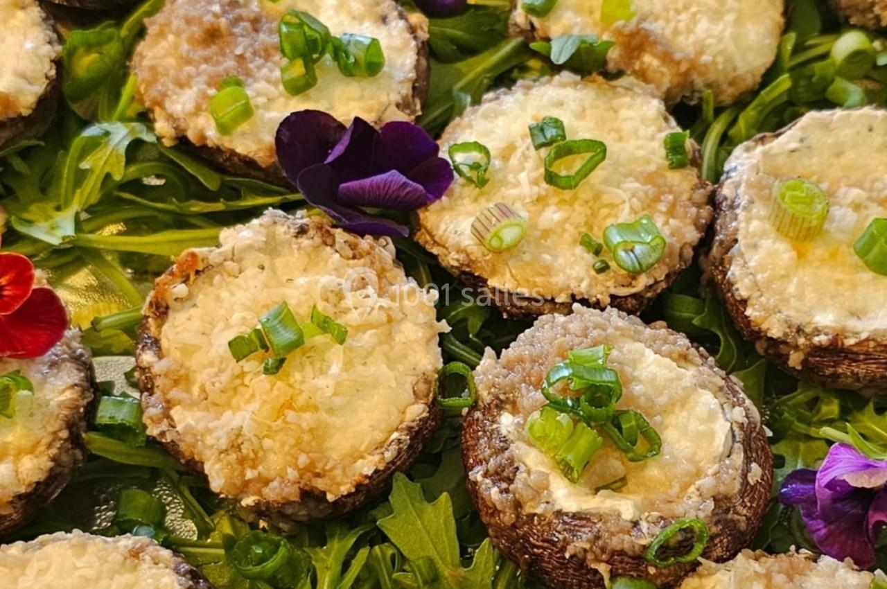 Champignons farcis gratinés sur un lit de roquette, garnis de ciboulette et de fleurs comestibles.