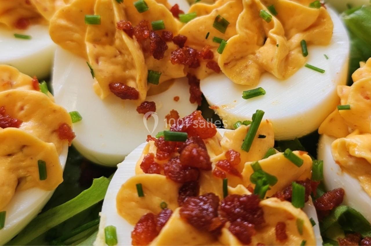 Œufs durs garnis de crème jaune, parsemés de morceaux de bacon croustillants et de ciboulette, sur lit de salade verte.